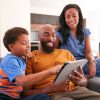 African American Family With Son Sitting On Sofa At Home Using Digital Tablet